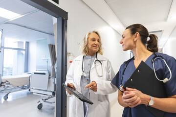 Happy caucasian female doctors with stethoscopes using tablet at hospital