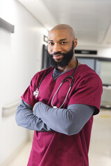 Portrait of happy african american male doctor wearing red scrubs in corridor at hospital