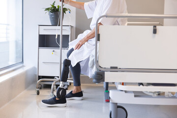 Midsection of senior caucasian female patient with prosthetic leg sitting on bed at hospital
