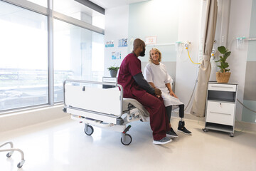 Senior caucasian female patient with prosthetic leg and african american male doctor sitting on bed