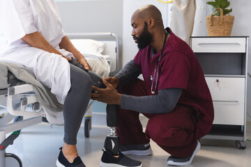 African american male doctor examining senior caucasian female patient with prosthetic leg - obrazy, fototapety, plakaty