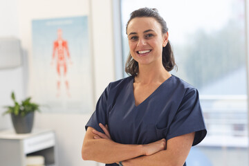 Portrait of happy female caucasian physiotherapist wearing scrubs at hospital - obrazy, fototapety, plakaty