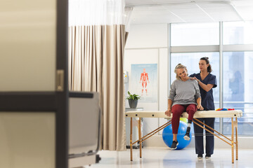 Fototapeta na wymiar Caucasian female physiotherapist and senior woman with artificial leg massaging back at hospital