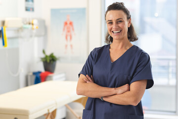 Portrait of happy female caucasian physiotherapist wearing scrubs at hospital