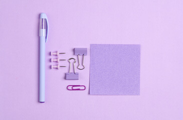 Blue stationery accessories on purple pastel background. Memo papers, pen, paper clips, pins. Monochrome objects. Flat lay. Top view