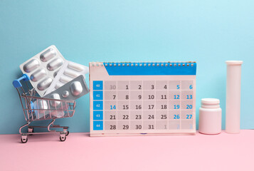 Desk calendar with blisters of pills in a supermarket trolley on a blue-pink pastel background