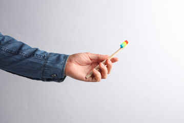 Man's hand in denim shirt holding rainbow wooden toothbrush on a gray background. Lgbt community