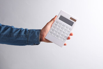 Hand in denim shirt holding calculator on a gray background. Business concept