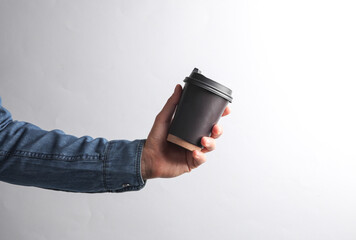 Man's hand in denim shirt holding brown paper coffee cup on a gray background
