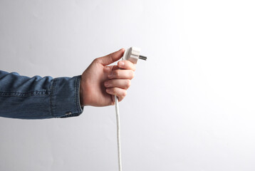 Man's hand in denim shirt holding electrical plug on a gray background