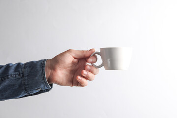 Man's hand in denim shirt holding ceramic cup on gray background