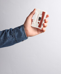 Man's hand in denim shirt holding retro audio cassette on a gray background