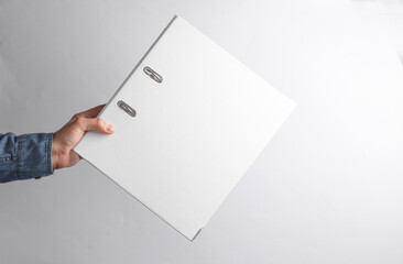 Man's hand in denim shirt holding white ring folder on gray background