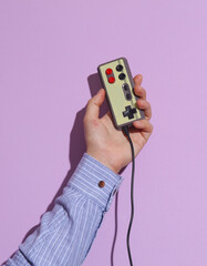 Man's hand in shirt holding retro joystick on purple pastel background with shadow.