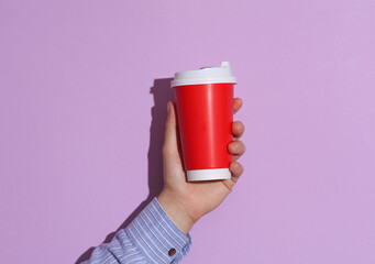 Man's hand in shirt holding red cardboard coffee cup on purple pastel background with shadow