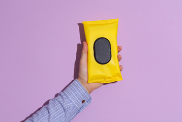Man's hand in shirt holding wet wipes package on purple pastel background with shadow.