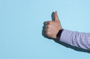 Man's hand in shirt with mart bracelet shows thumbs up on blue background with shadow