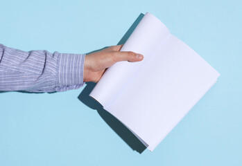 Man's hand in shirt holding open white blank magazine mockup on blue background with shadow