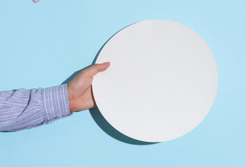 Man's hand in shirt holding white round on blue background with shadow