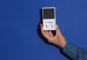 Man's hand in denim shirt holds wooden block calendar organizer with date December 11 on a blue...