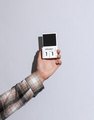 Man's hand in shirt holds wooden block calendar organizer with date january 11 on gray background with shadow