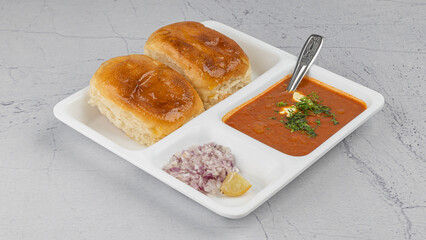 Indian Mumbai Street style Pav Bhaji, garnished with peas, raw onions, coriander, and Butter. Spicy thick curry made of out mixed vegetables served with pav over textured background with in white plat