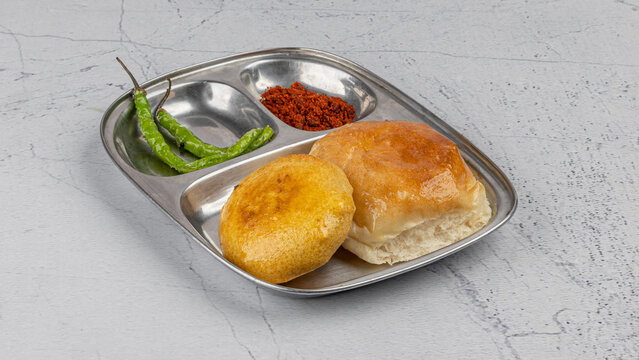Vada Pav or Vada Paav with chutney is a famous Indian street food in steel plate on whote textured background