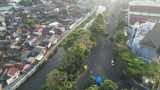  Aerial view of Misty Jogja City with vehicles traffic in the foggy morning sunlight. Resident's house settlement on the edge of the code river with trees around in Yogyakarta.