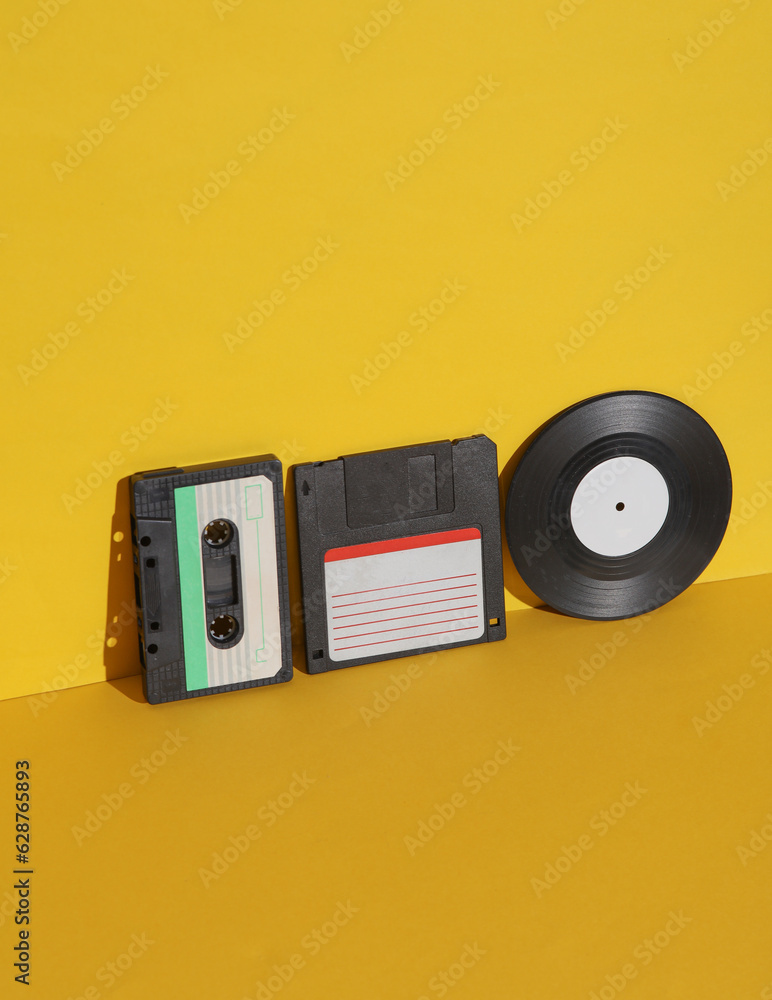Poster outdated technologies. retro 80s audio cassette with floppy disk and vinyl record on yellow backgrou