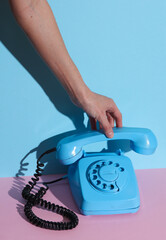 HAnd holding Blue Rotary retro rotary telephone handset on pink blue background with shadow. Creative layout