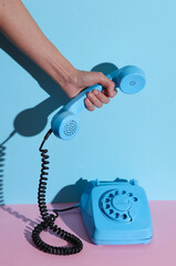HAnd holding Blue Rotary retro rotary telephone handset on pink blue background with shadow. Creative layout