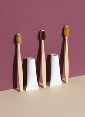 Eco wooden toothbrushes and tubes of toothpaste on burgundy beige background with shadow. Beauty concept