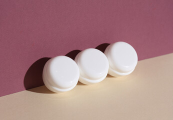 White cream jars on burgundy beige background with shadow. Creative beauty layout. Mockup, template for design