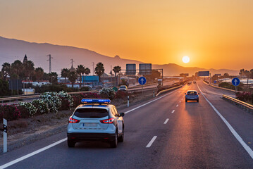 Traffic police car driving on a highway with the early morning sun rising over the mountains on the horizon.