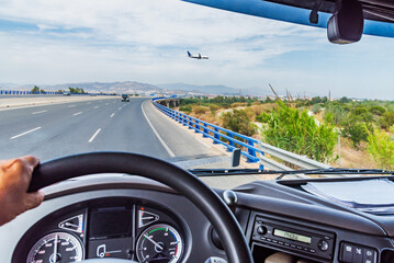 View from inside the cabin of a truck driving on a highway and a plane flying low over the road.