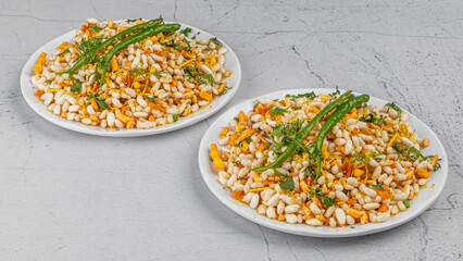 Bhelpuri is a savoury snack or chaat. It is made out of puffed rice, vegetables, tangy tamarind sauce, sukhi bhel in white plate with chilies garnished