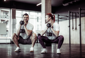 Fototapeta na wymiar Athletic man and woman squat together with dumbbells in a modern gym. Healthy lifestyle, Bodybuilding and fitness