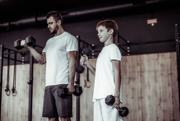 Healthy family concept. Father trainer and teenager son training with dumbbells in gym. Fitness,...
