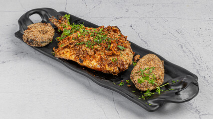 Pomfret fish tawa fry garnished with lemon and onion in a black ceramic plate with marble background,selective focus