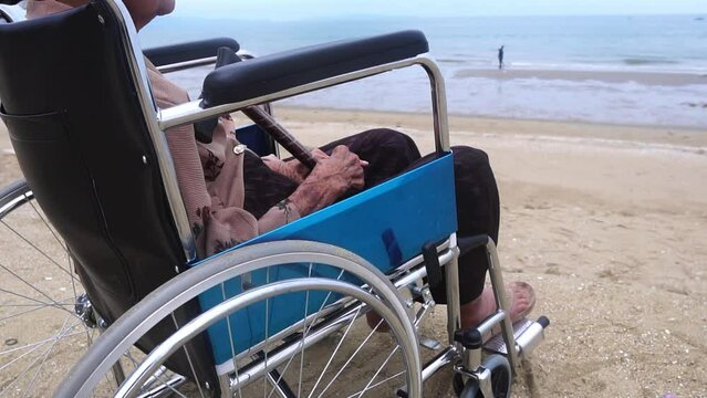 Fotage Slow Motion: Senior asian woman siting on wheelchair looking out on Beach