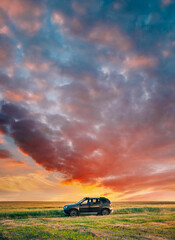 AWD 4WD SUV green car in summer meadow landscape in summer field countryside landscape. Sunset sky background.