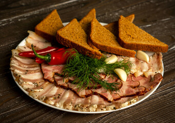A plate of sliced pork ham and bacon with bread and garlic