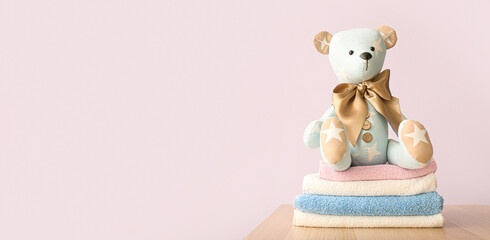 Bear toy with baby clothes on table against light color background. Banner for design