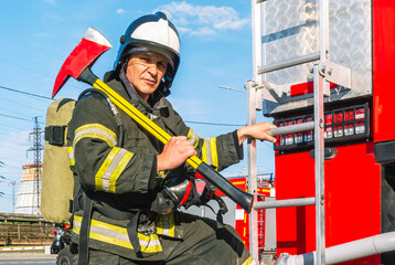 A firefighter in a helmet and breathing apparatus put an assault axe on his shoulder. A firefighter...