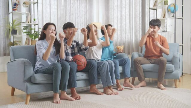 Asian Teenagers Cheering And Watching Basketball Game On Tv And Celebrating Victory At Home
