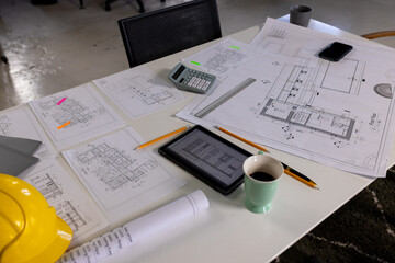 Overhead view of desk with architectural blueprints, tablet, coffee and hardhat