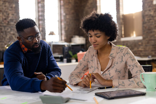 Focused diverse male and female architects discussing blueprints sitting at desk in office