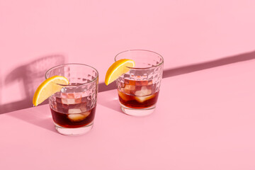 Glasses of rum with ice cubes and lemon slices on pink background