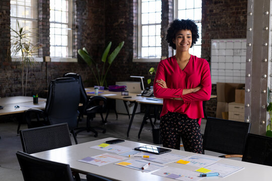 Portrait of happy biracial casual businesswoman standing in office smiling, copy space