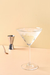 Glass of martini with ice, bar spoon and jigger on beige background